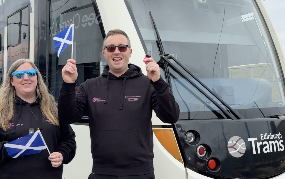 Emma and Jason holding Scotland flags in front of a tram