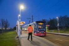 an image of a tram at a tram stop with a person wearing orange high-vis stood on the platform