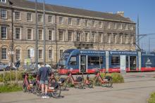 A tram at Picardy Place with a man standing next to Voi bikes at the forefront of the image