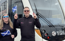 Emma and Jason holding Scotland flags in front of a tram
