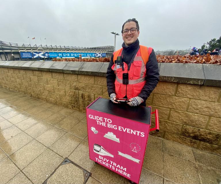 Ticketing Service Assistant selling tickets on the plaform at Murrayfield tram stop.