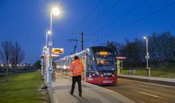 an image of a tram at a tram stop with a person wearing orange high-vis stood on the platform