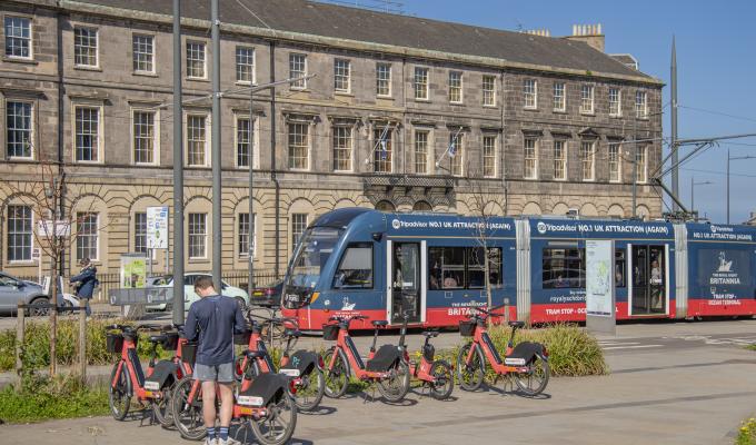 A tram at Picardy Place with a man standing next to Voi bikes at the forefront of the image