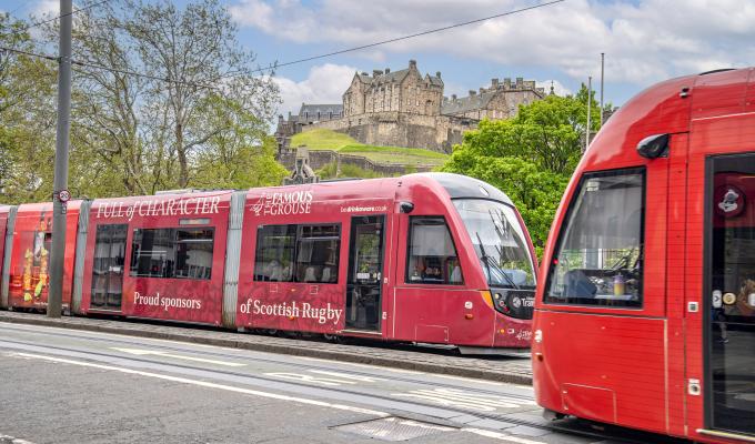 Two trams passing each other on Princes Street with Edinburgh Castle in the background